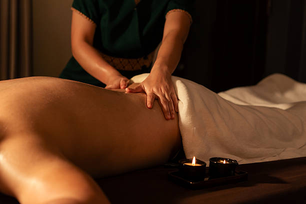 istock Wellness spa a male client, lying face-down on a massage table, is receiving a therapeutic back massage. professional masseuse massage on back a customer with warm oil from a melted massage candle. 2227408213