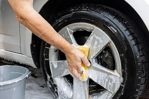 istock Man's arm with soapy yellow sponge cleaning alloy wheel 2227410661