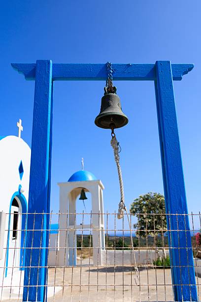 Bell at Agios Charalambos Chapel in Kefalos, Kos, Greece, showcasing its distinct blue and white design with a rustic bell against a bright summer sky