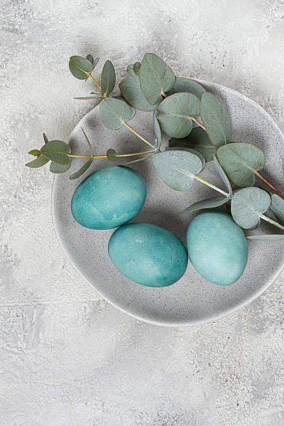 istock Easter colored eggs, in turquoise tones, on a gray plate, with a branch of eucalyptus, Easter card, top view, no people 2227415281