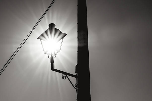 The sun shines intensely through an urban streetlight, creating a starry effect that symbolizes the fusion of natural energy and technology. This conceptual image represents the use of solar energy as a source of sustainable lighting in urban environments. (renewable energy, technological innovation, and urban sustainability) Edited in black and white. Copy space