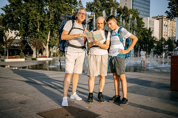 Grandfather, father and son traveling together with backpacks as a tourists in the city standing on town square and looking at map for directions