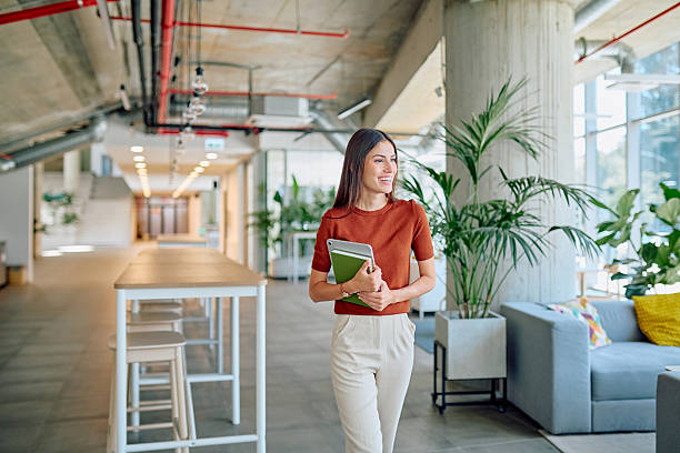 istock Young businesswoman walking in a modern office holding tablet and notebook 2227426007