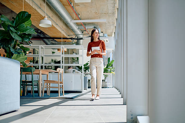 istock Young businesswoman walking through modern office holding digital tablet 2227426049