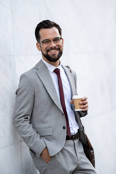 istock Smiling businessman holding coffee and leaning against wall 2227427480
