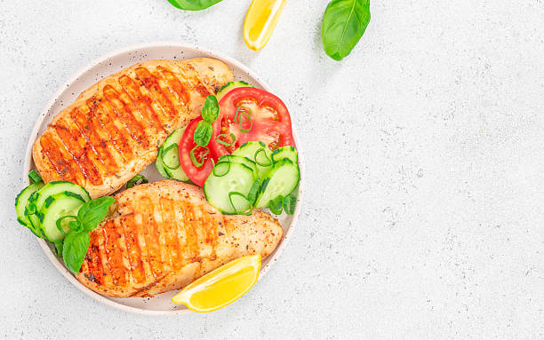 istock Grilled chicken breast with fresh vegetables and lemon on white plate. top view. copy space 2227428833