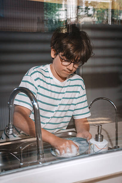 istock Young boy washing dishes in kitchen sink with sponge 2227433835