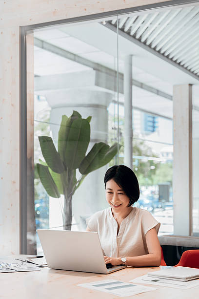 istock Focused mature eastern business woman working on laptop computer sitting at office workplace desk. Asian entrepreneur manager businesswoman finance analyst using pc for data analysing. Vertical 2227434509