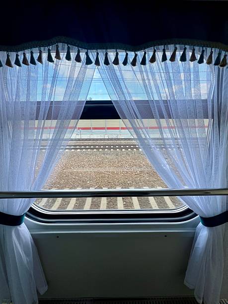 view from inside a train, looking out through a window adorned with white sheer curtains and tassels, revealing train tracks