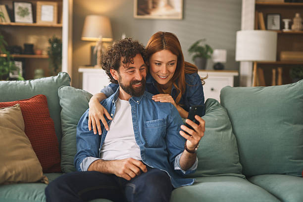 istock Happy couple relaxing on sofa browsing smartphone at home 2227441029