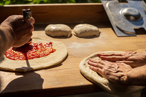 Artisan hands preparing pizza dough and spreading tomato sauce