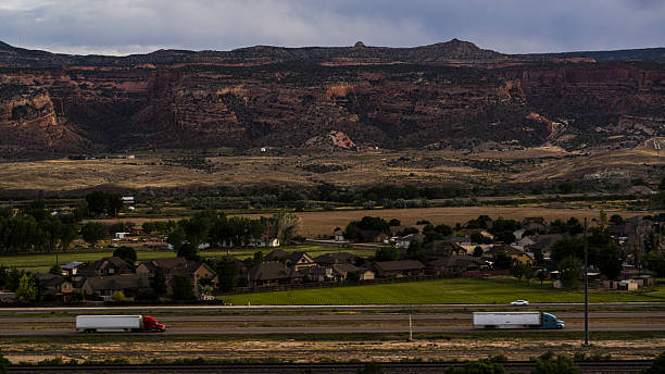istock Trucks passing through valley. Homes at base of dramatic mesa cliffs in Fruita, Colorado. 2227444901