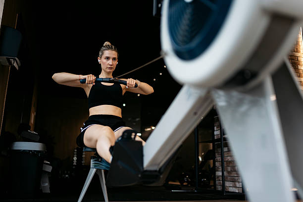 Determined sportswoman exercising using rowing machine at fitness center