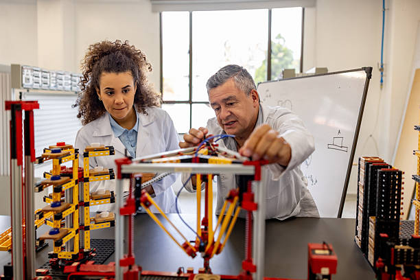 Latin American teacher showing a female engineering student how to assembly a model in a robotics class - STEM concepts