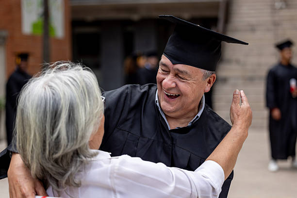 Senior wife hugging her husband on his graduation ceremony and looking very happy - education concepts