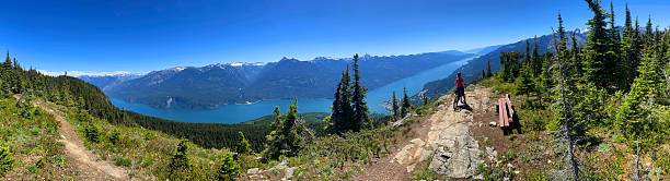 A female mountain bike rider looks at the view of Kaslo and Kootenay Lake from Mt. Buchanan Lookout in British Columbia, Canada, on a summer's day.