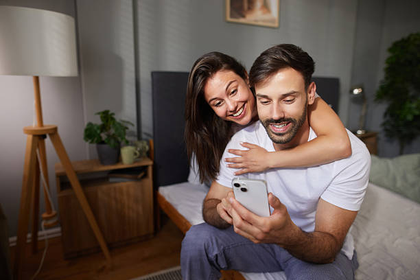 istock Happy couple sharing a moment of joy while using smartphone in bedroom 2227448929
