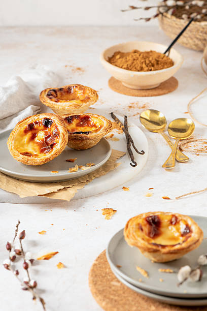 istock Several Pastel de Nata are arranged on plates with cinnamon, vanilla beans, and small golden spoons. 2227451603