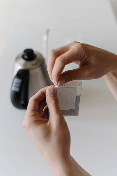 Close-up vertical cropped shot of male hands opening single-serve drip coffee bag, preparing to brew fresh cup of coffee with modern method at home in morning.