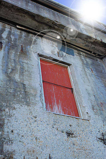 Red shuttered window on a weathered concrete wall under a bright sky