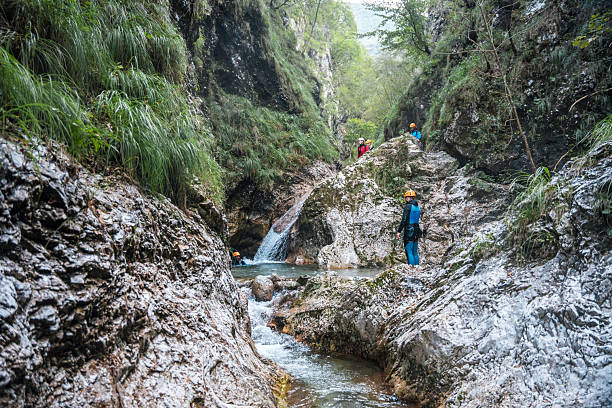 Geared up in neoprene suits and safety helmets, diverse friends enjoy outdoor fun as they walk through canyons during a thrilling canyoning expedition.