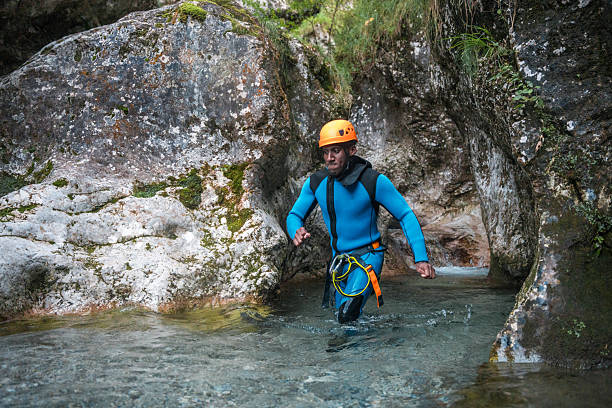 A black male in a neoprene suit and safety helmet, walking and enjoying the water canyoning.