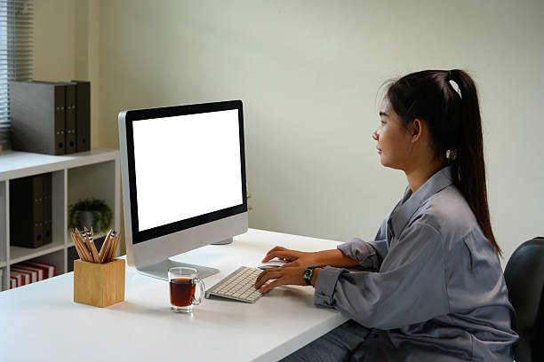 istock Young woman working on desktop computer with blank white screen, sitting at a modern office 2227475792