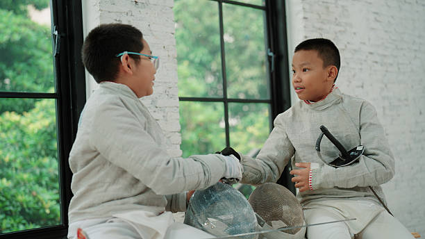 Two young fencers greeting each other with their gloves on, ready to begin the match.