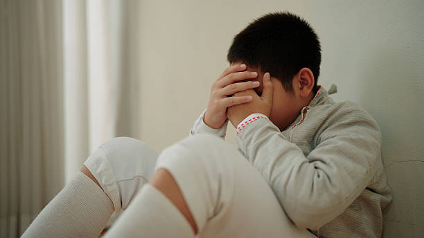istock Stressed young boy sitting quietly on the floor with his hands touching his head 2227479149