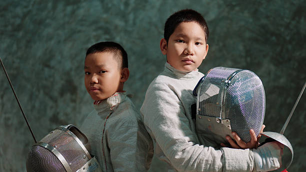 Two young fencers stand proudly, looking confidently into the camera.