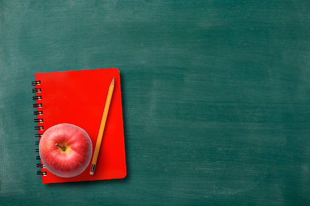 Spiral notebook, apple and pencil on blackboard with copy space