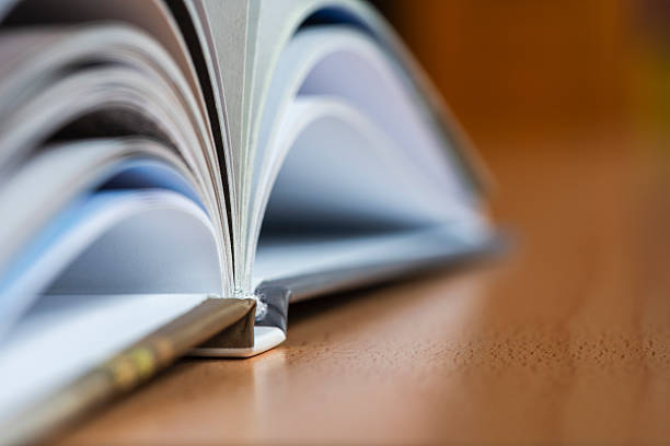 istock Open book lying on a desk with a blurred view of a bookshelf in the background, object with selective focus 2227487522