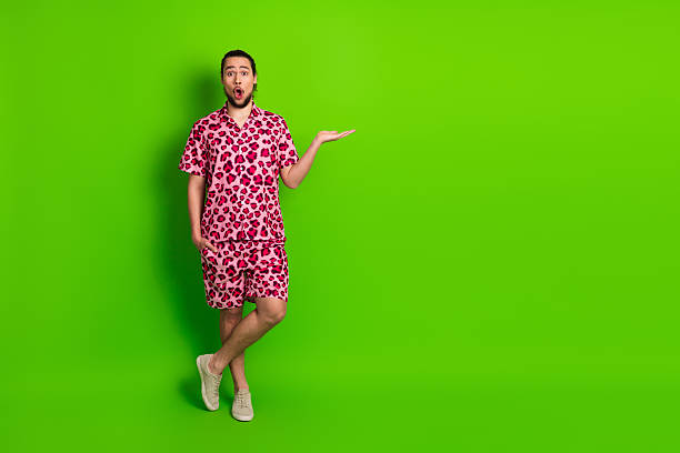 istock Young man in stylish pink leopard print outfit posing against a solid green background, expressing surprise 2227492782