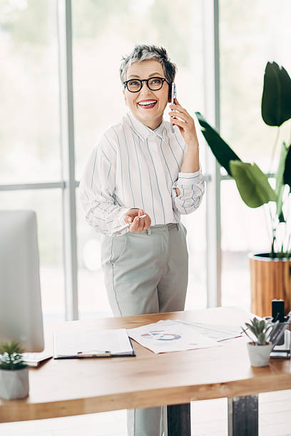 istock Professional mature businesswoman using a smartphone in a modern office environment with creative documents and desk items 2227497283