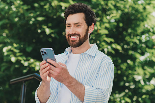 istock Handsome man smiling while using a smartphone outdoors in sunny weather surrounded by greenery 2227498309