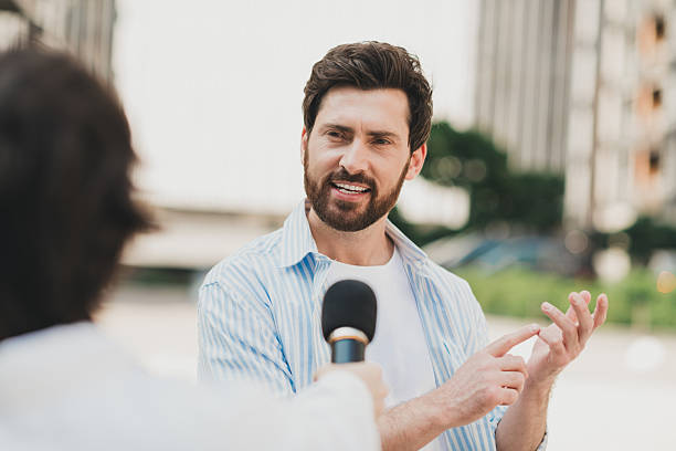 istock Confident young man speaks passionately into a hand-held microphone during an outdoor discussion on a sunny day 2227498373