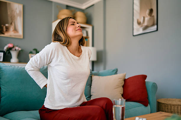 istock Woman suffering from back pain while sitting on sofa at home 2227503014
