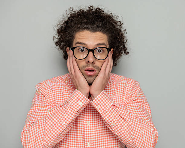 istock surprised attractive guy with glasses holding palms on face and opening mouth 2227509209