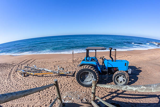 Cromer, Norfolk, United Kingdom: October 18, 2024: A bright yellow but rather rusty beach tractor on a slipway on the beach at Cromer in North Norfolk, Eastern England, on a sunny autumn day. The tractor has pulled a fishing boat up the beach from the surf, with the day’s catch of crabs and lobsters. Cromer is famous for crustaceans.