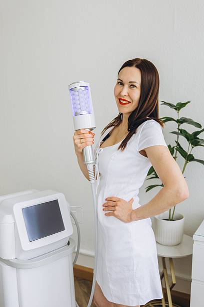 istock Smiling cosmetologist holding device for Microvibration Therapy. Professional body contouring equipment in modern aesthetic clinic. Anti-cellulite treatment concept 2227514975