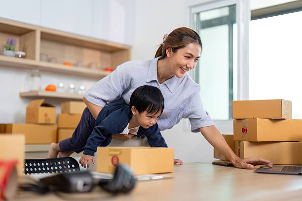 istock Playful Learning. Mother helping child explore laptop while balancing on packages. 2227516435