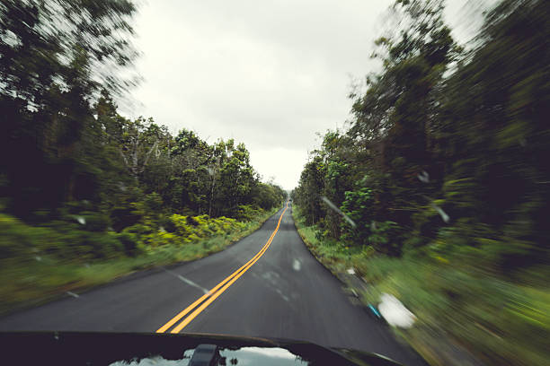 View through windscreen of a car travelling along a green tree lined road on Hawaii
