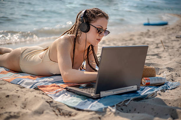 A digital nomad with dreadlocks enjoys beachfront serenity, using her headphones and laptop to unwind with a mix of music, creativity, and sunshine