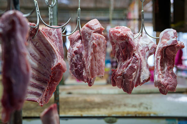 Close-up of raw pork cuts hanging on metal hooks at a traditional meat market stall.