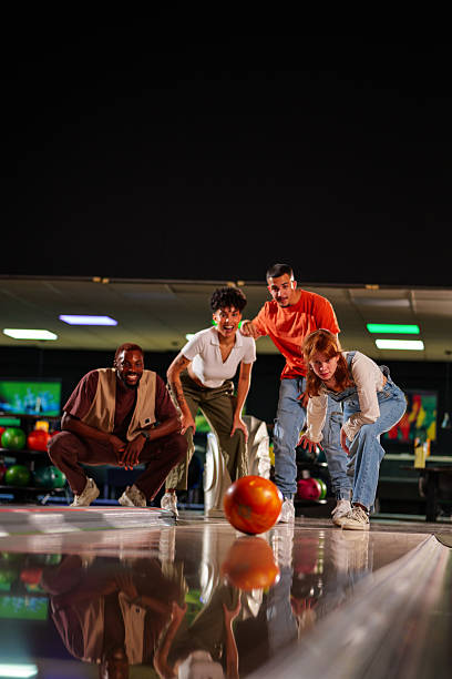 istock Four friends crouching and cheering joyfully as a bowling ball rolls down the polished lane, creating an atmosphere of excitement and support 2227524408