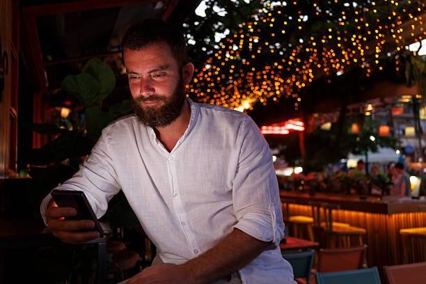 Handsome Caucasian man using smart phone while relaxing in a cafe on a night out while on vacation