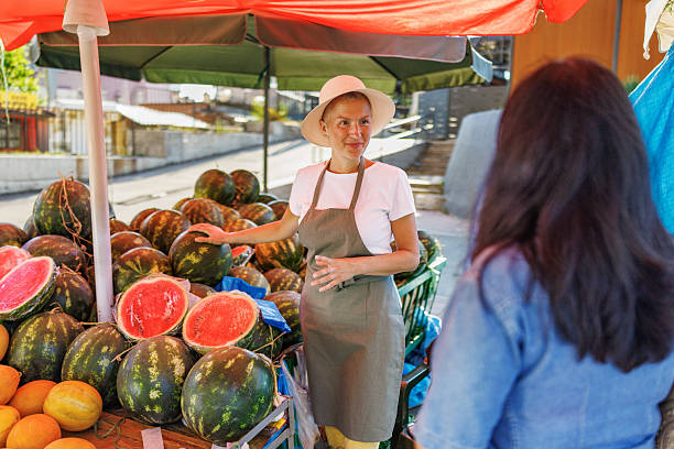 Warm exchange at a produce stall where a vendor offering a watermelon, encouraging the customer to check its weight and sound