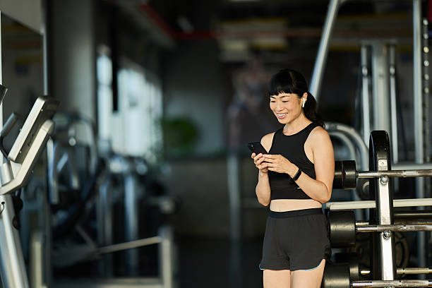 istock Smiling Woman in Gym Using Smartphone During a Rest Between Workouts 2227544255