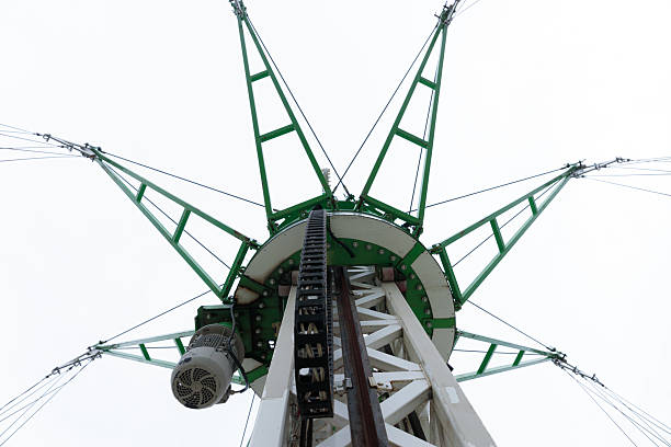 This image captures the towering structure from a ground-up perspective, revealing intricate green support beams, cables, and a motor in a cloudy atmosphere.