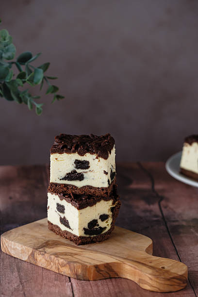 Delicious layered cheesecake with chocolate crust and cookie pieces on a wooden board in a cozy setting